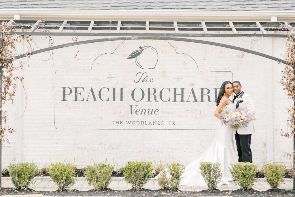 Bride and groom posing in front of The Peach Orchard venue sign.