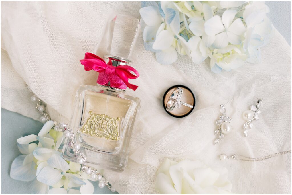 Wedding details including perfume, earrings, peal necklace and wedding rings.