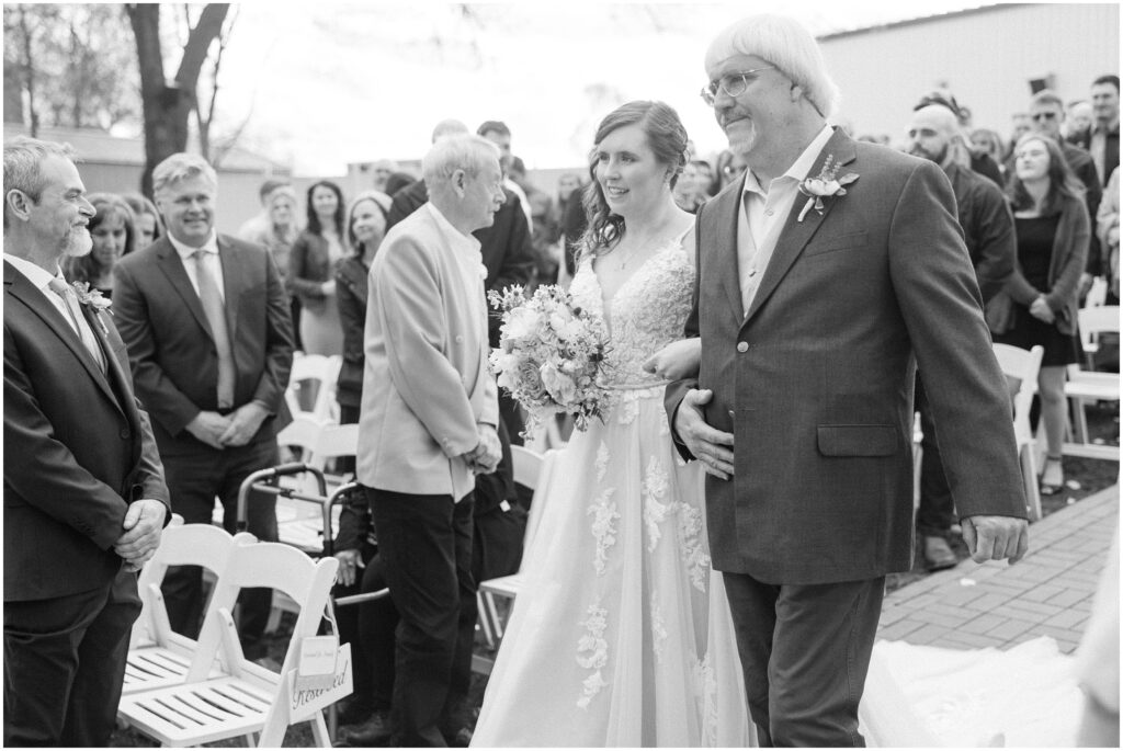 Black and white photo of bride being walked down the aisle by her father.
